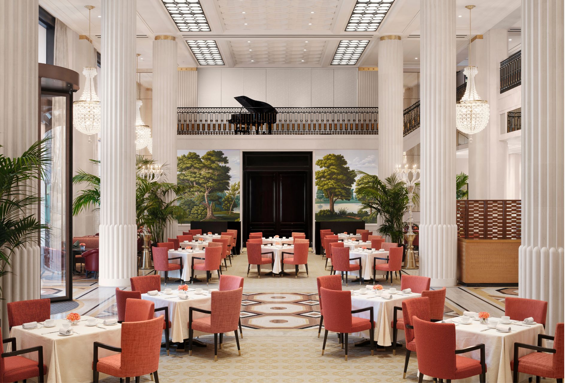 Hotel lobby with red chairs, white tablecloths and a mezzanine level with a grand piano.