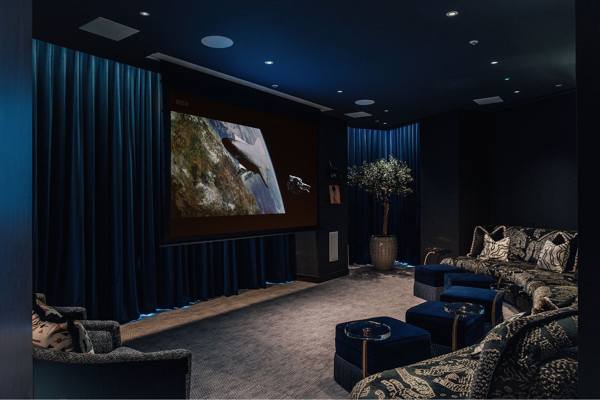 Screening room with navy blue walls and black velvet sofas with navy velvet footstools