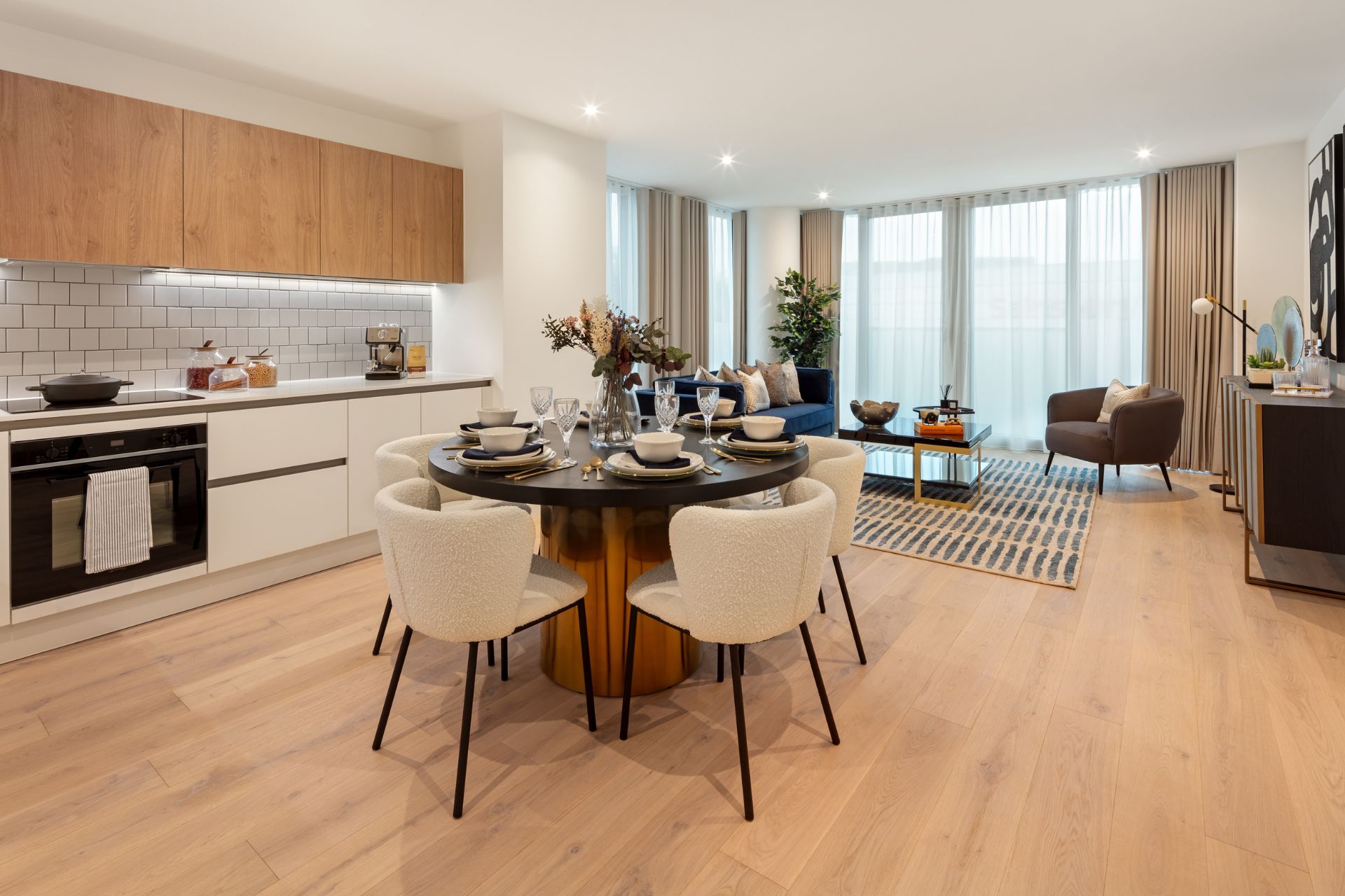 Open-plan kitchen/dining area with white dining chairs, white units and floor-to-ceiing windows