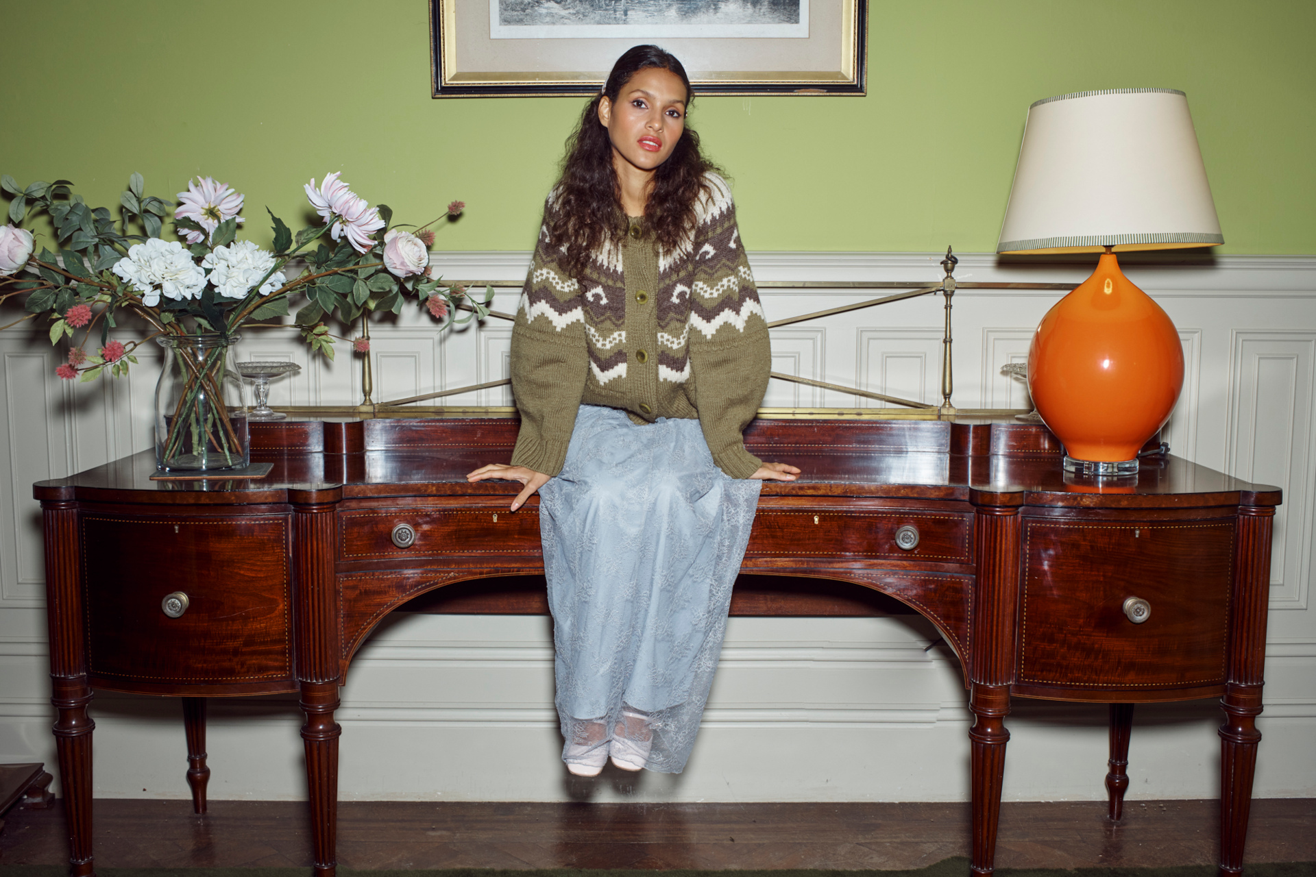 Woman in green knit and blue skirt sitting on side table