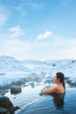 The girl bathes in a hot spring in the open air with a gorgeous view of the snowy mountains.