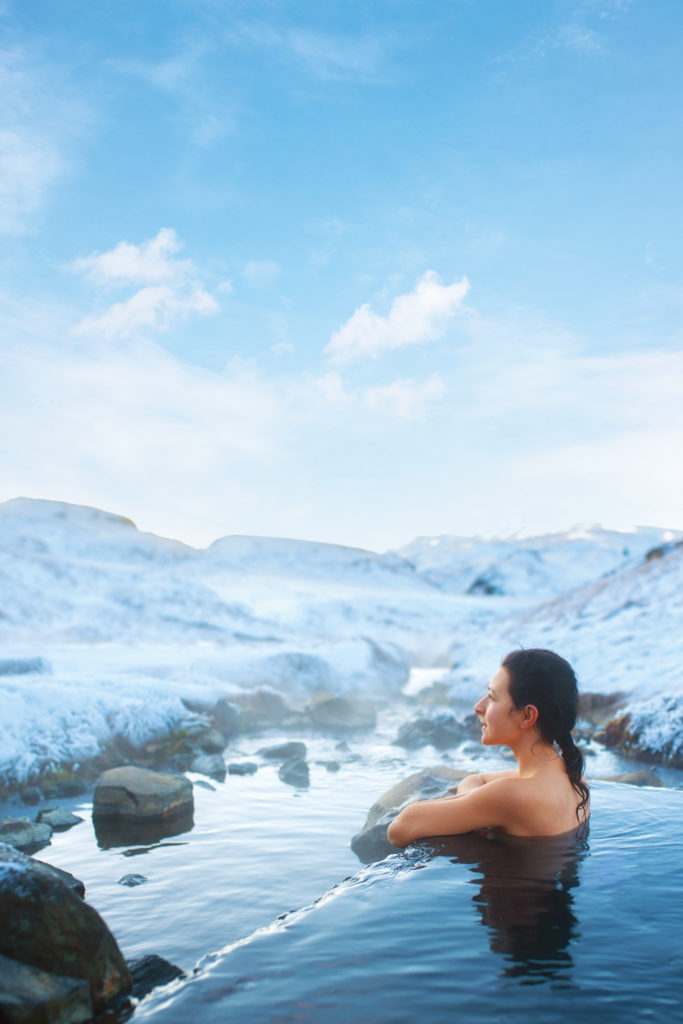 The girl bathes in a hot spring in the open air with a gorgeous view of the snowy mountains.