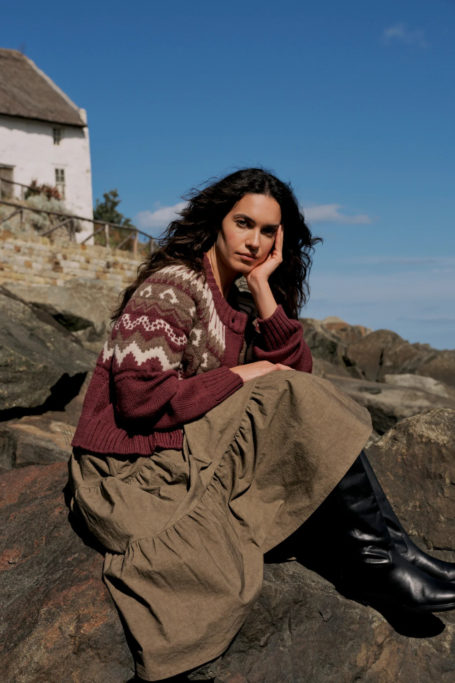 Woman in Fair Isle jumper and long skirt sat on rock
