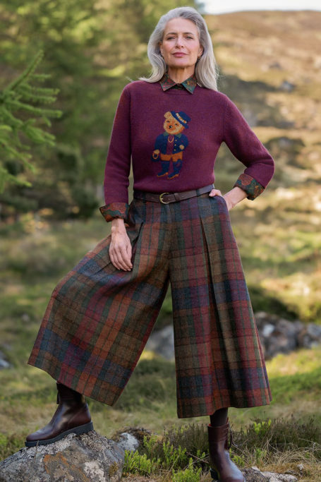 Woman stood in field wearing tartan trousers and knitted jumper