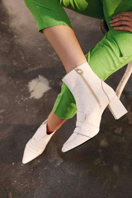 Close up of woman's bottom half, wearing green trousers and white boots