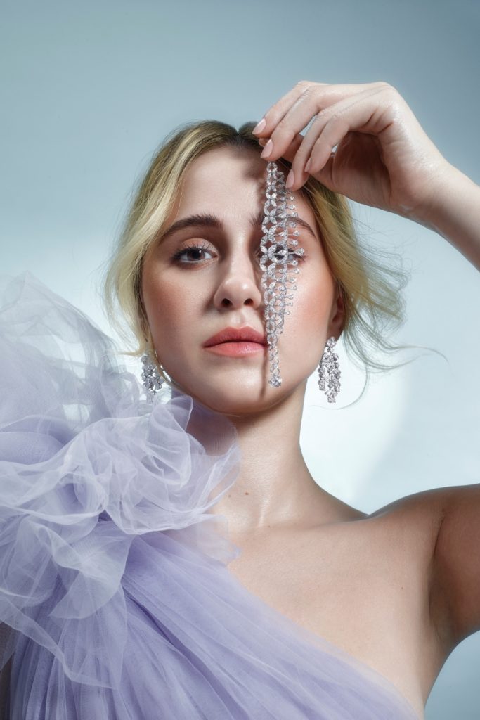 Maria Bakalova holds diamond jewellery in front of her eye