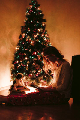 A girl reading a book beside a Christmas tree