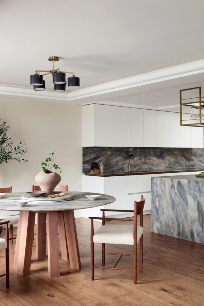 Kitchen with grey marble island. white cabinets and a marble table with wooden legs