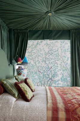 Green four poster bed with white sheets, a pink bedspread and pale blue floral wallpaper.