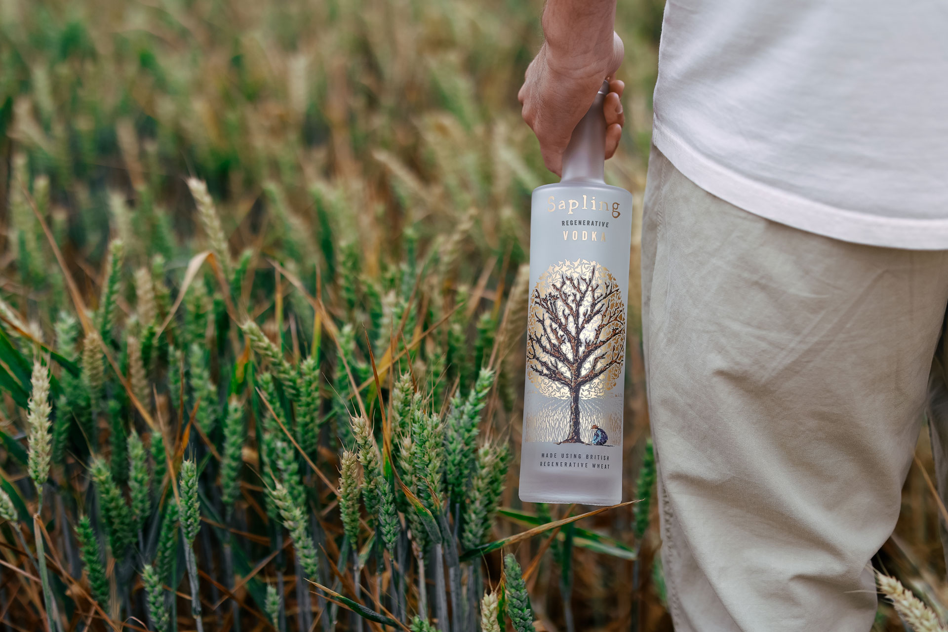 Man holding a bottle of Sapling Spirits in a field