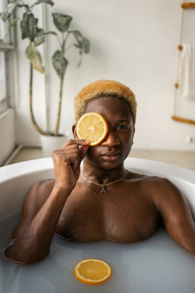 Man in bath holding orange slice in front of his eye | men tweakment trends 2025
