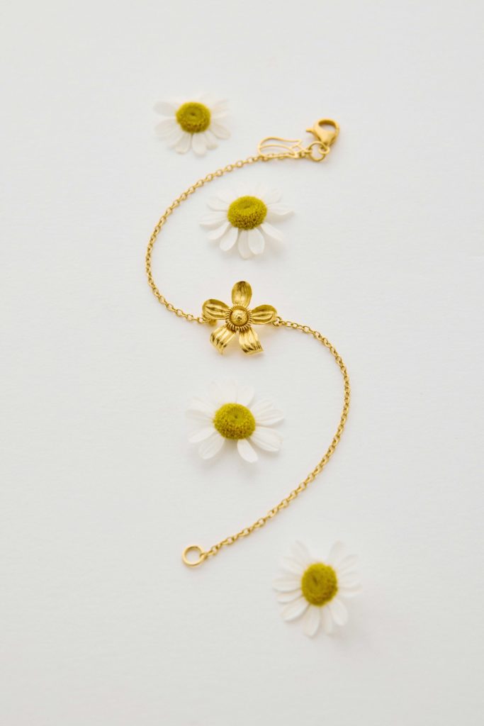 Gold bracelet with flower on a table with daisies