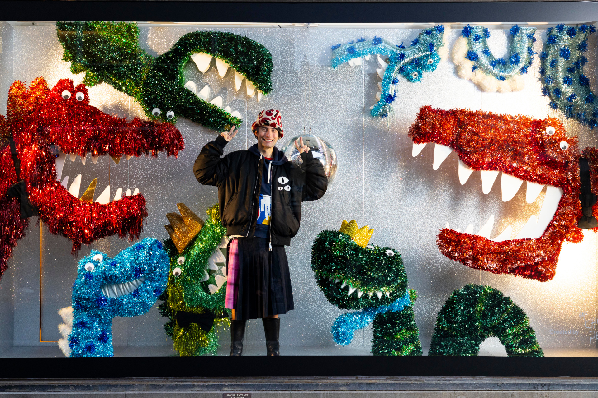 Tinsel creatures in shop window with man stood pointing at them