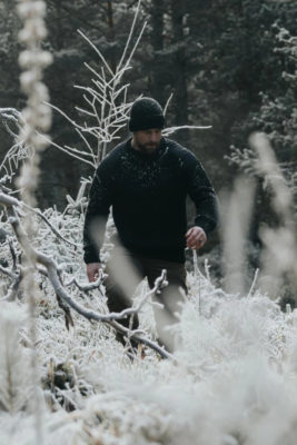 Man in black jumper walking through snowy forest
