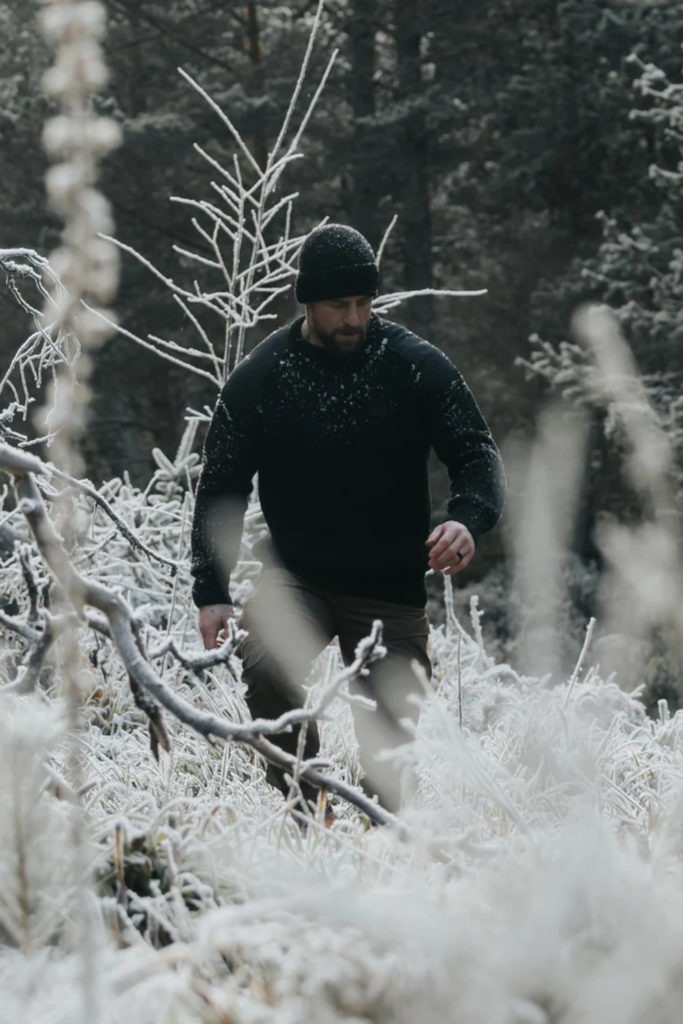 Man in black jumper walking through snowy forest