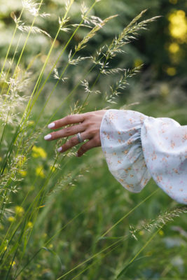 Hand with engagement ring brushing through grass in field