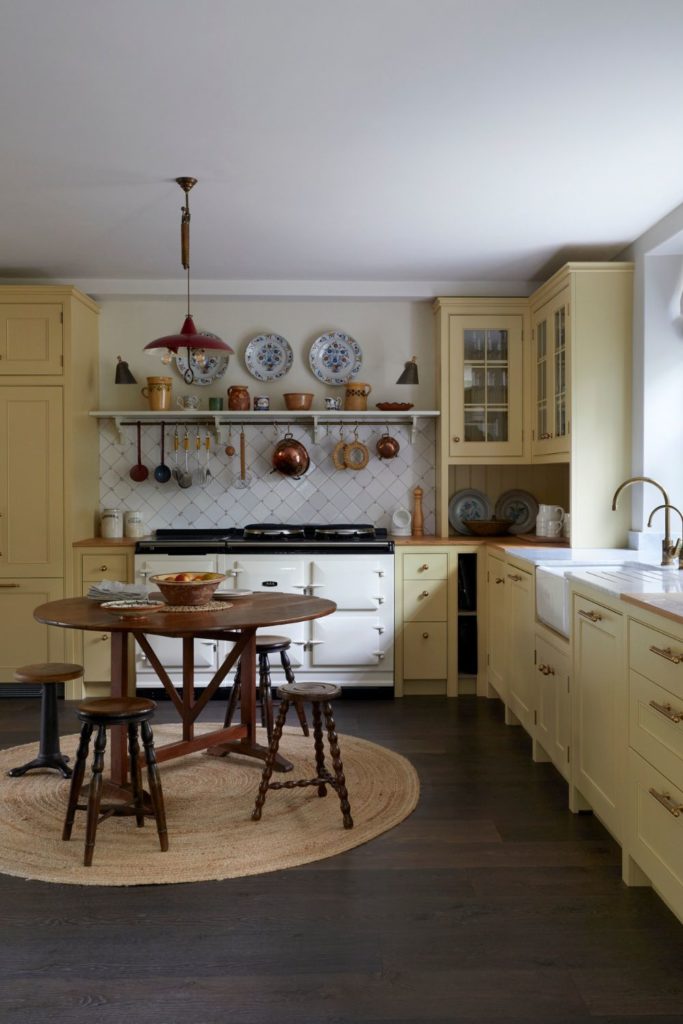 Pale yellow kitchen with white counters and a dark wooden circular dining table with a rattan rug