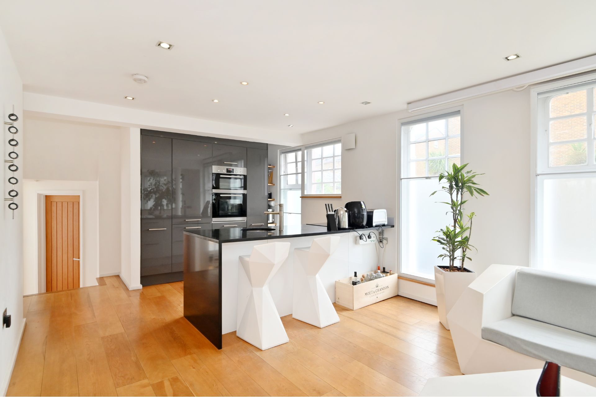 Open plan kitchrn with white cabinets, black countertops and geometric white bar stools