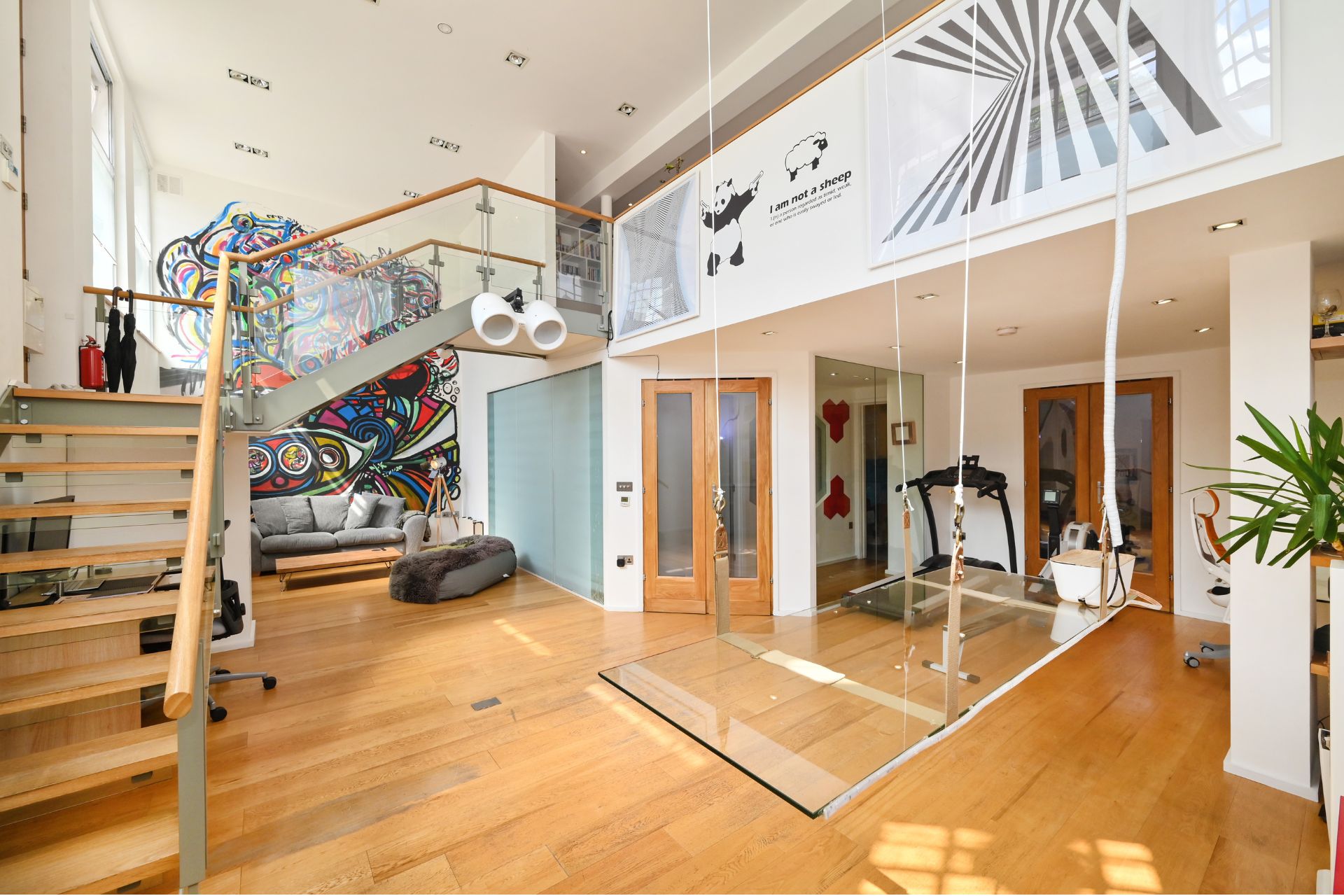 Loft-style living room with wood and glass staircase and a glass panel used to hold a DJ deck