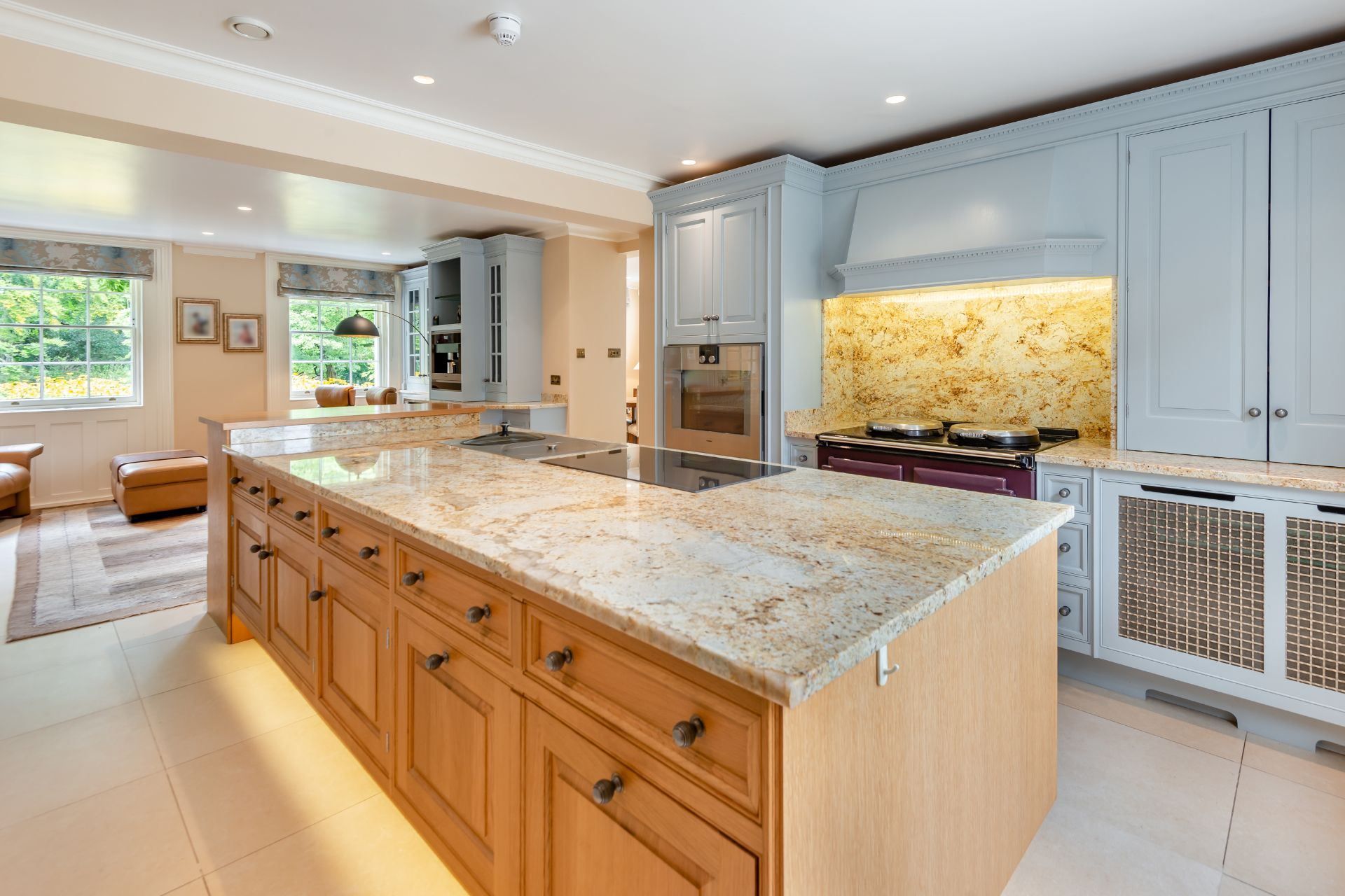 Kitchen with wooden cabinets, a marble-topped island and large windows.