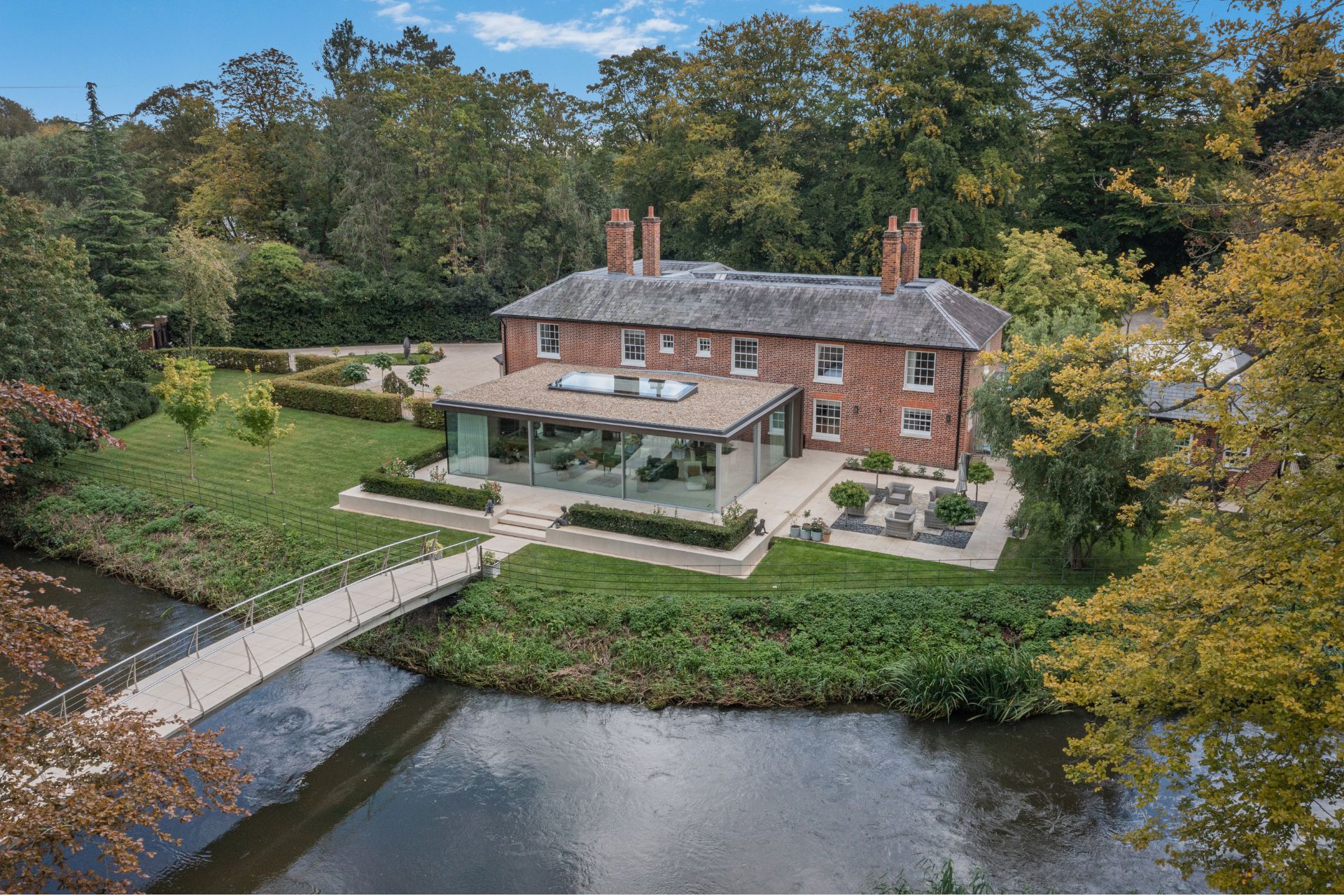 Georgian red brick house with large glass extension and a steel bridge over a waterway.