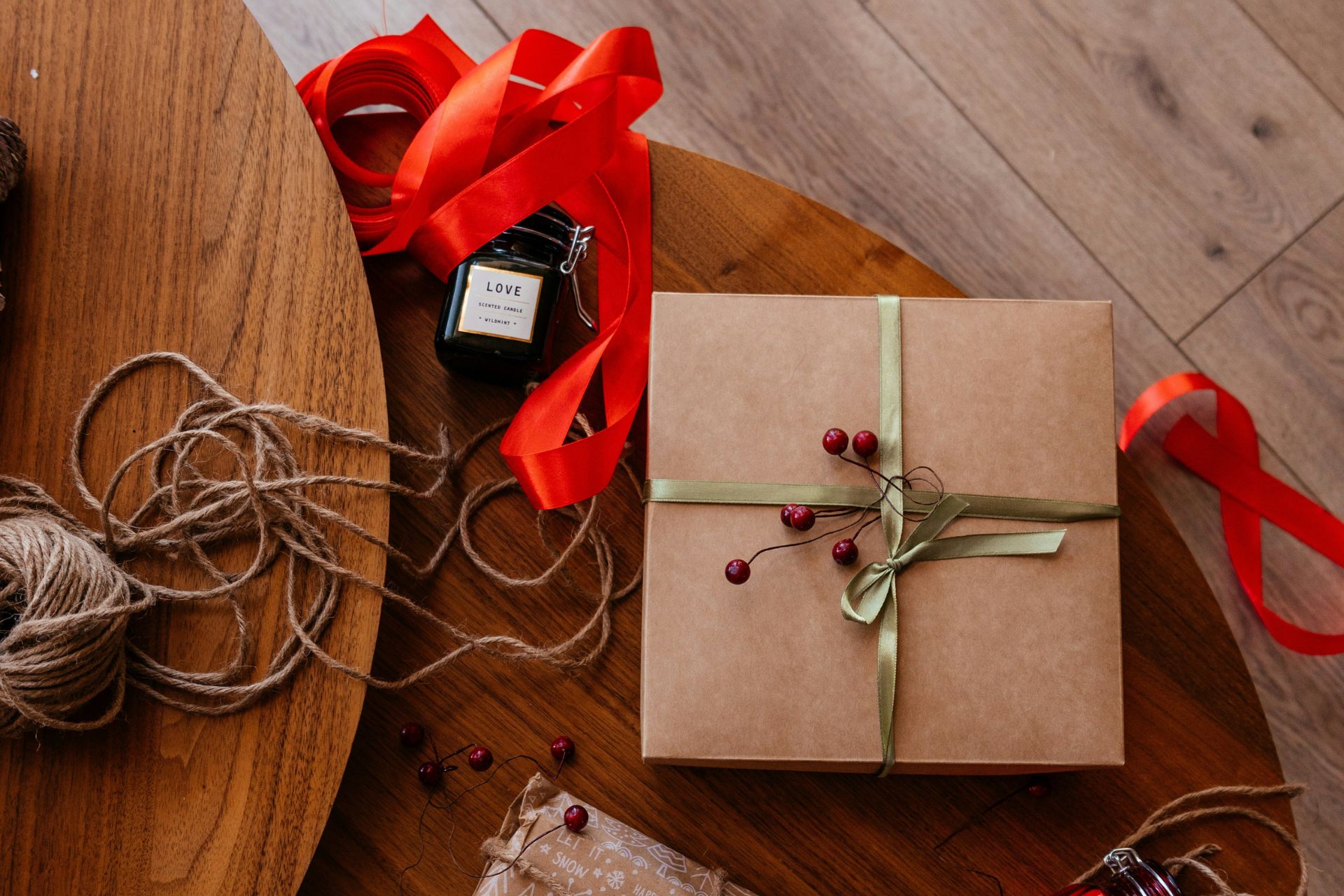 Christmas presents wrapped in brown paper, positioned next to rolls of twine and red ribbon