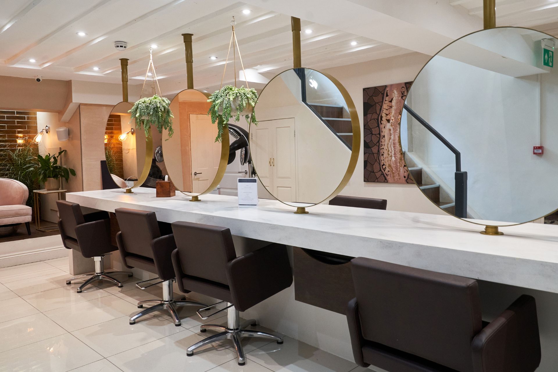 Modern hair salon with dark brown leather chairs and large round gold-framed mirrors