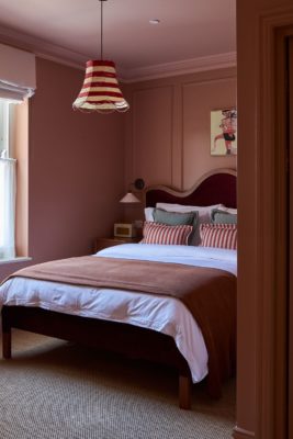 Dusty pink bedroom with a burgundy curved headboard and a matching bedspread.