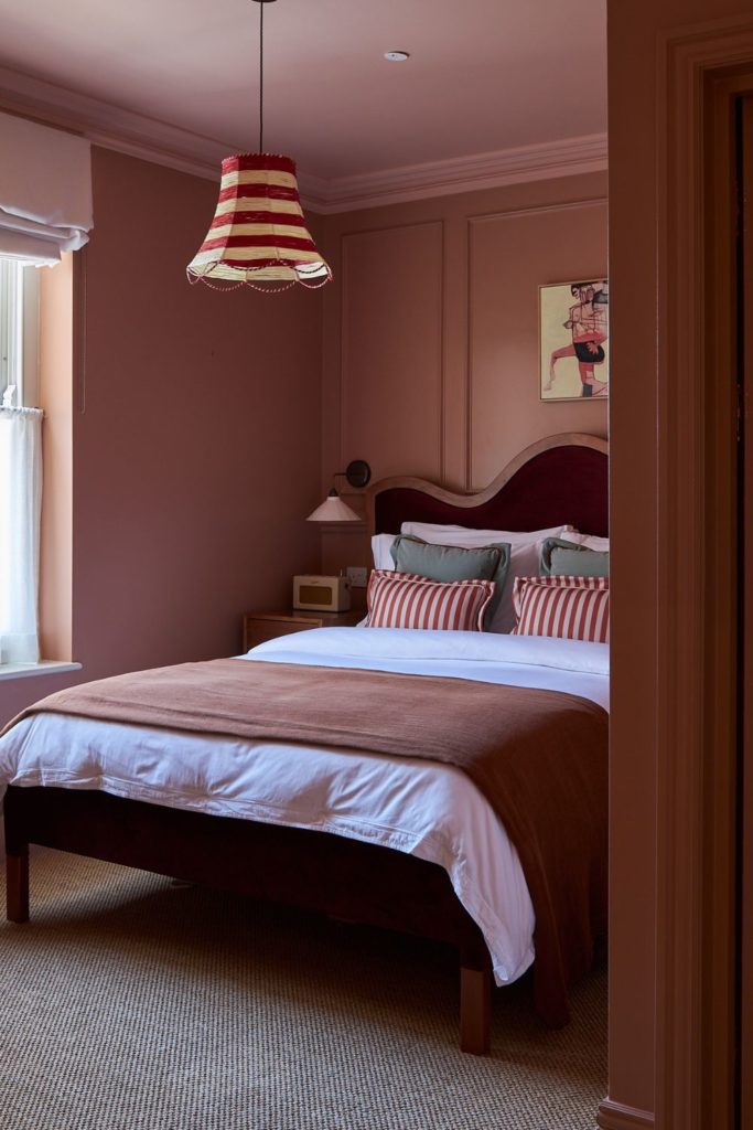 Dusty pink bedroom with a burgundy curved headboard and a matching bedspread.