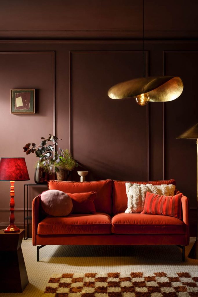 Burgundy panelled living room with a red elvet sofa and gold floor lamp