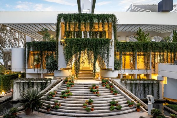 Modernist home with semicircular steps leading to an arched doorway draped with foliage