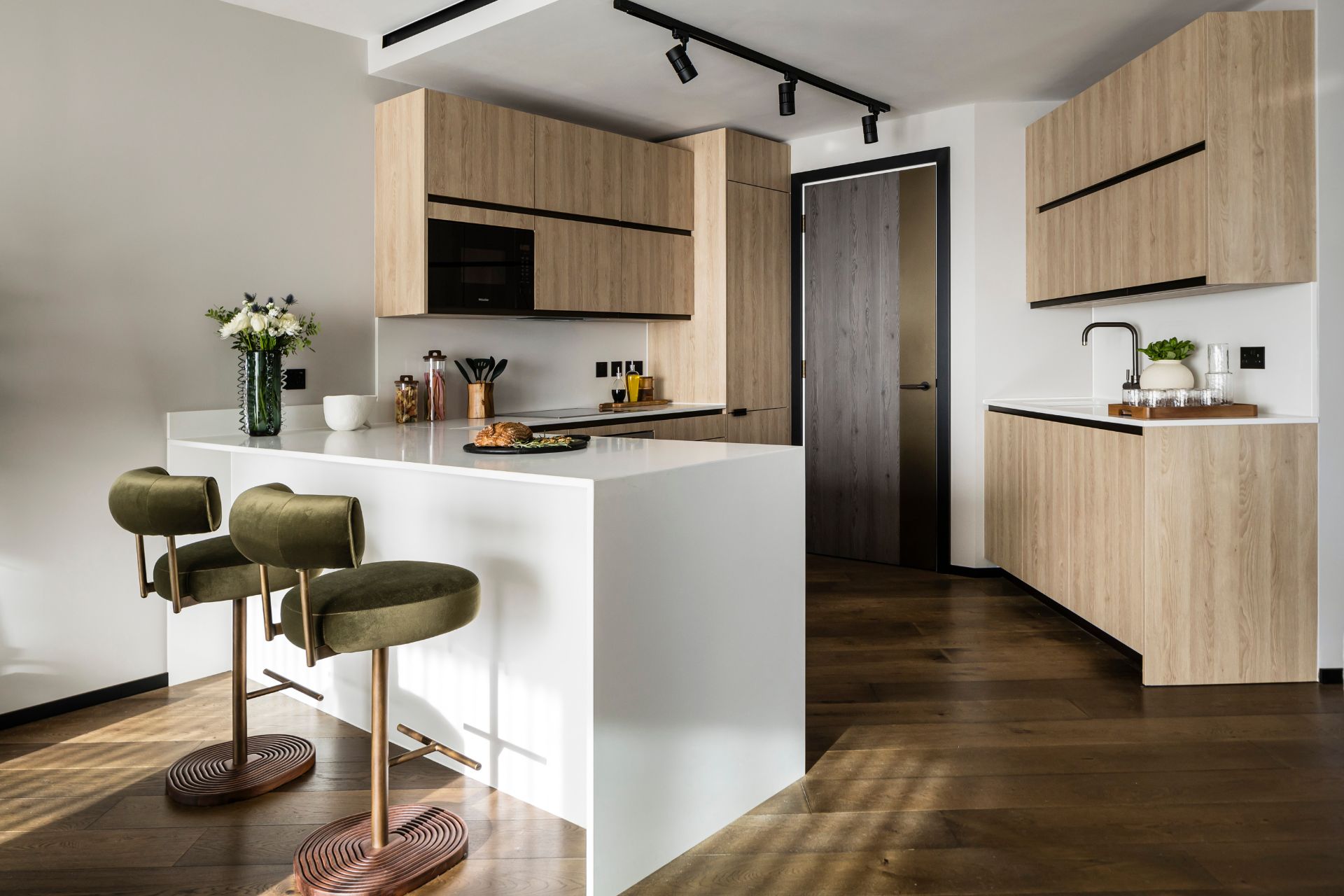 Modern kitchen with pale oak cabinets, white island and green velvet bar stools