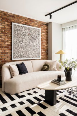 Living room with curved cream sofa, black and white rug and exposed brick wall