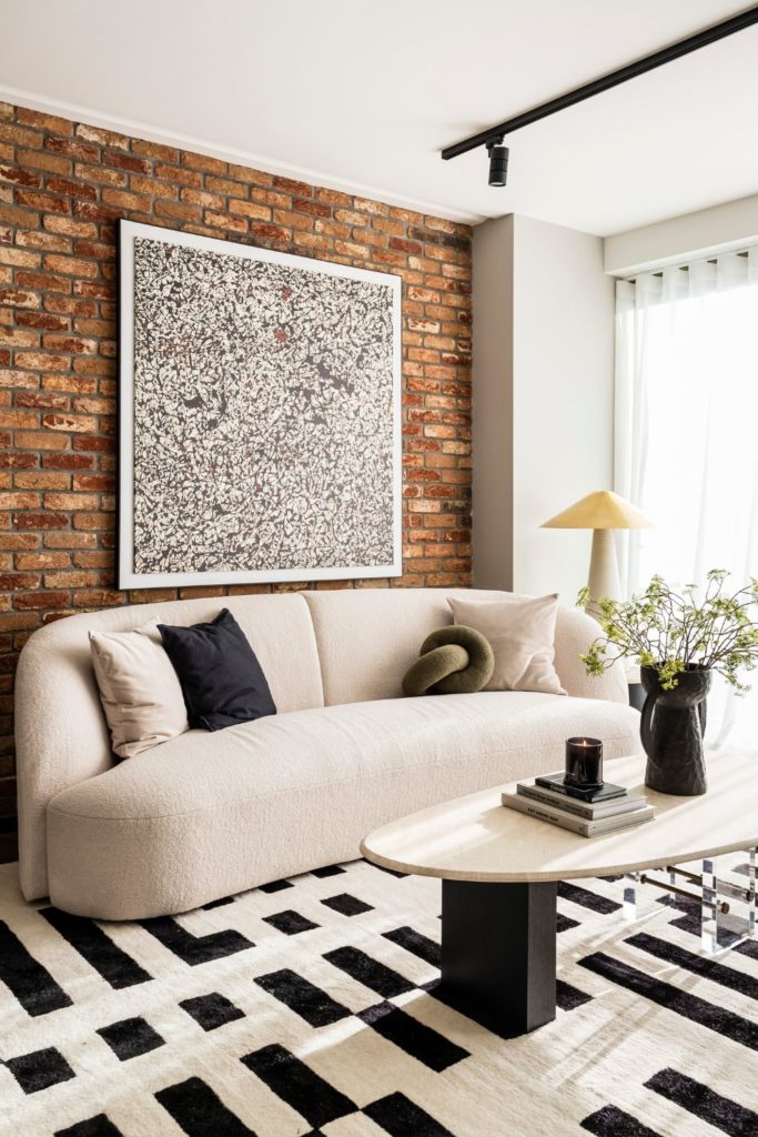 Living room with curved cream sofa, black and white rug and exposed brick wall