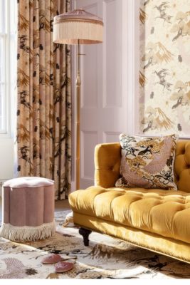 Mustard yellow velvet sofa with a pale pink velvet pouffe, pink and cream patterned wallpaper and patterned curtains