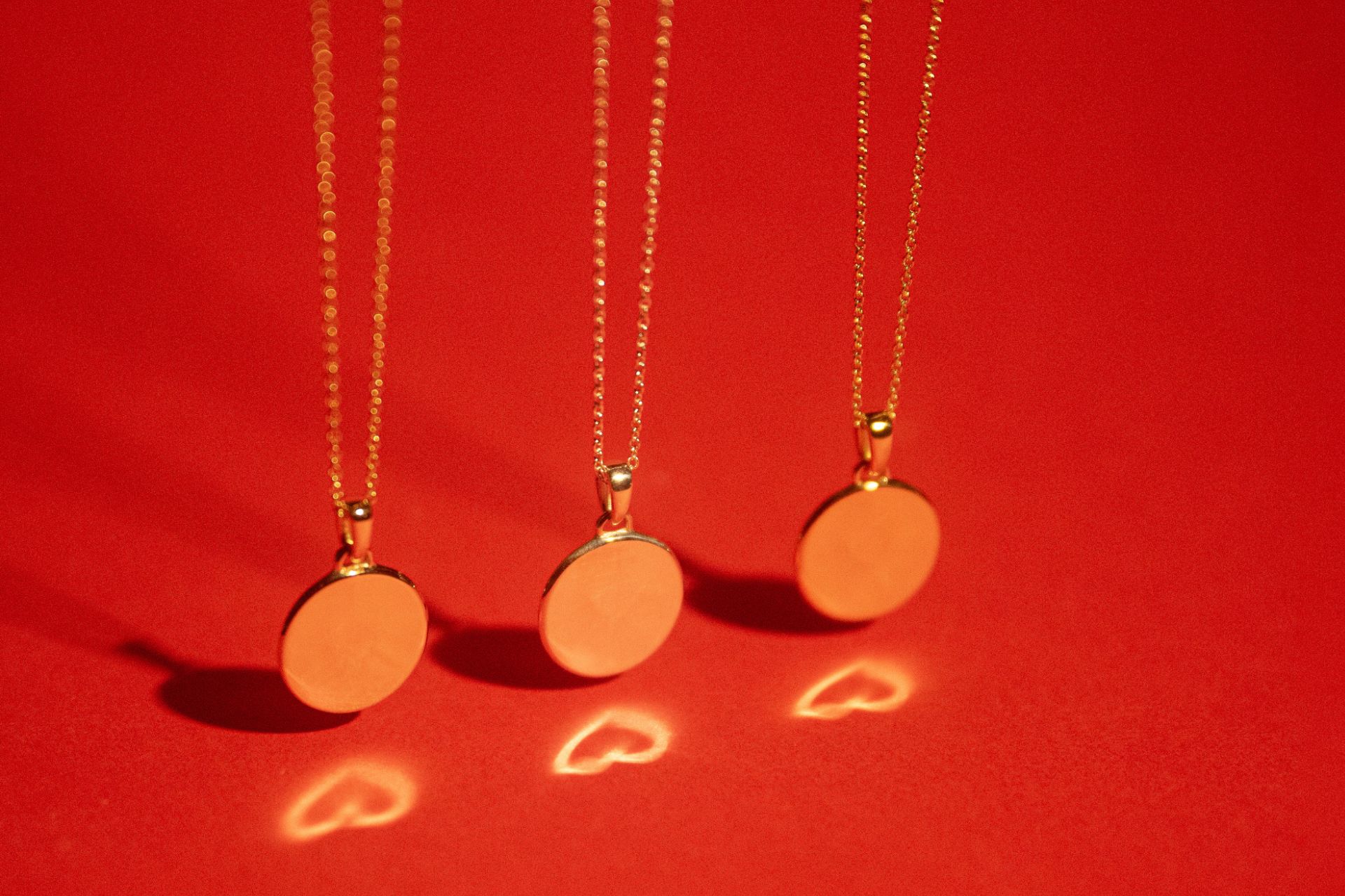Gold circular pendant necklaces reflecting heart shapes onto a red background