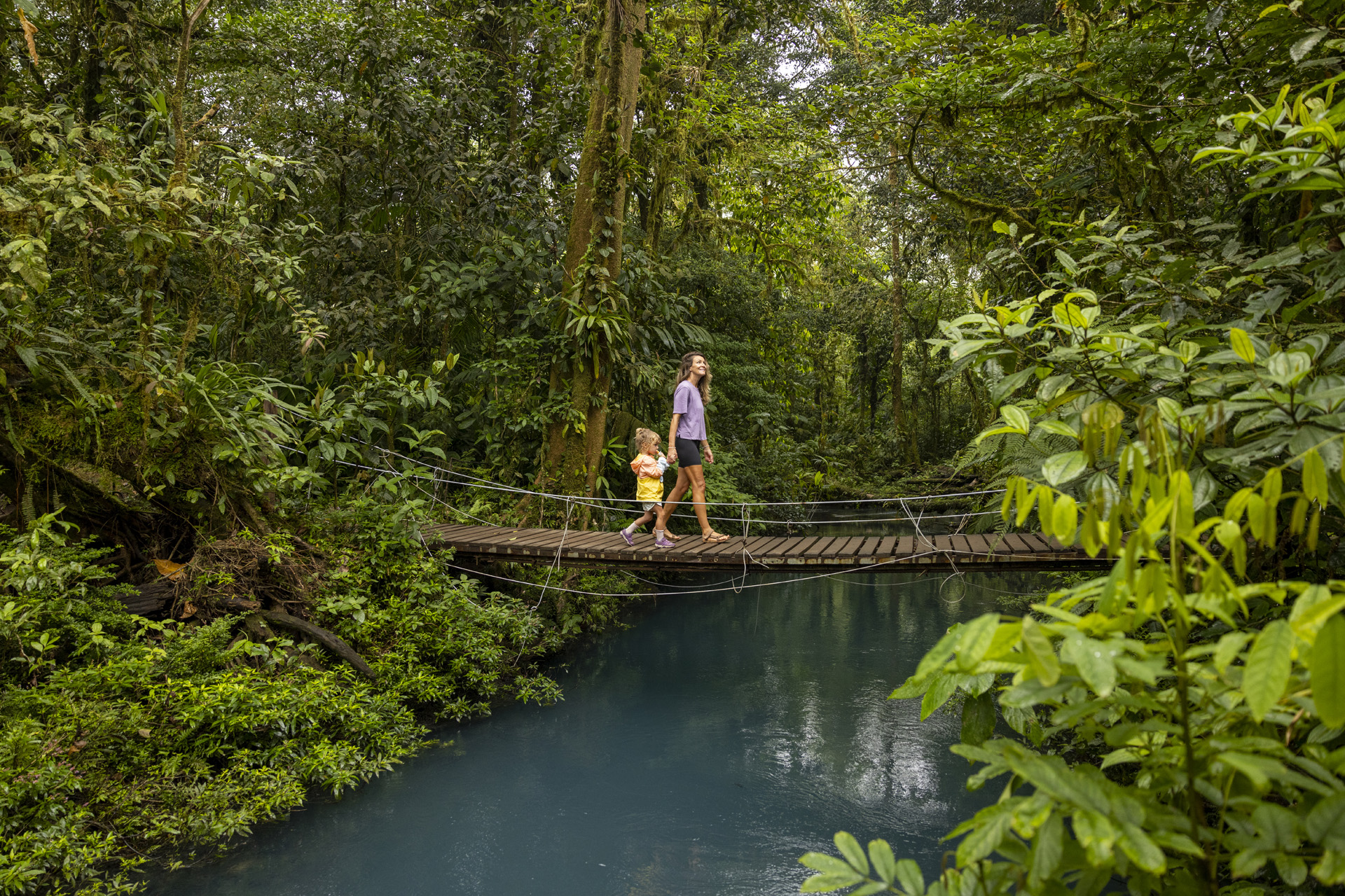 A woman hiking with her daughter across a bridge in Costa Rica.