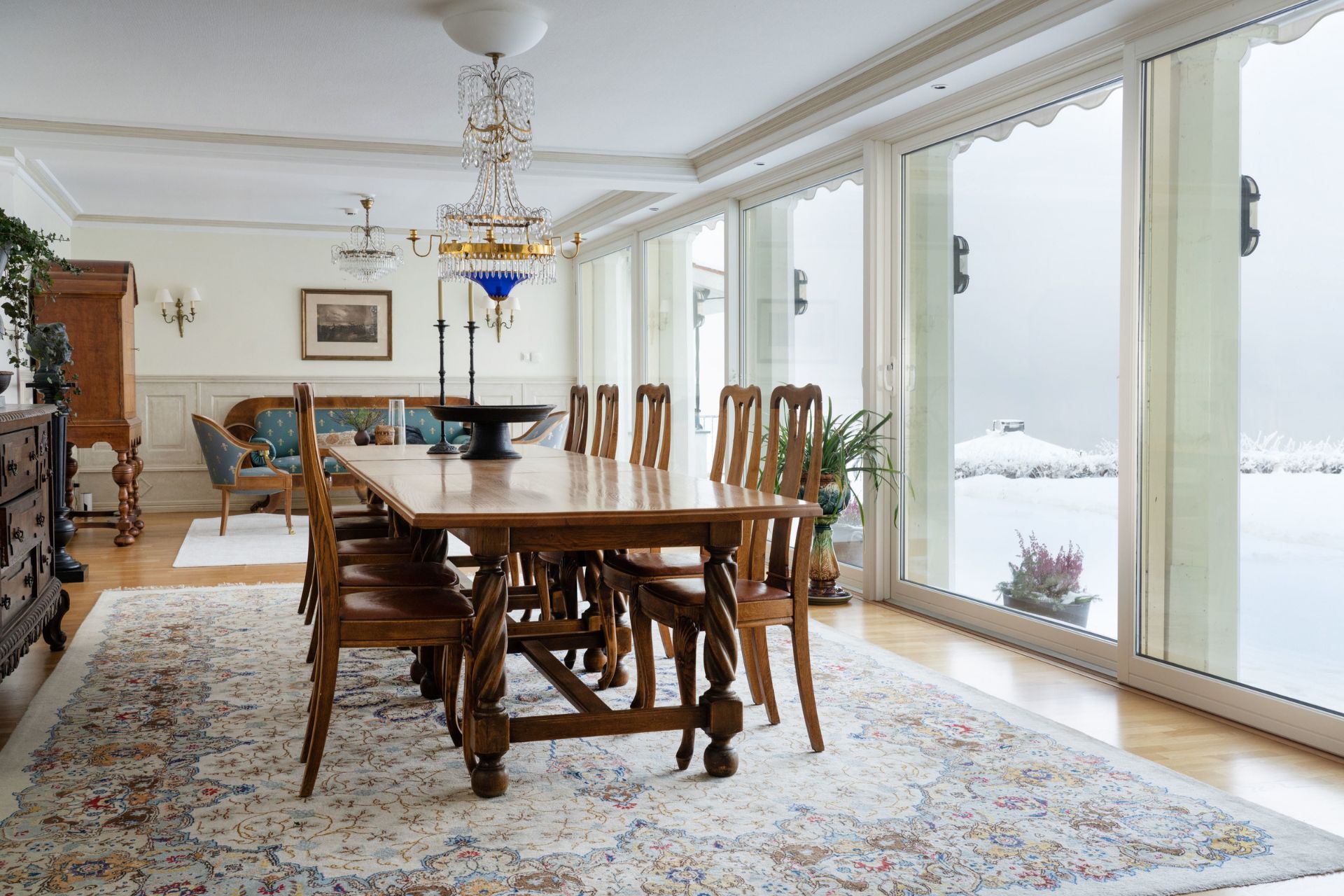 Dining room with wooden furniture, a taupe floral rug, and floor-to-ceiling sliding glass doors overlooking a stone terrace