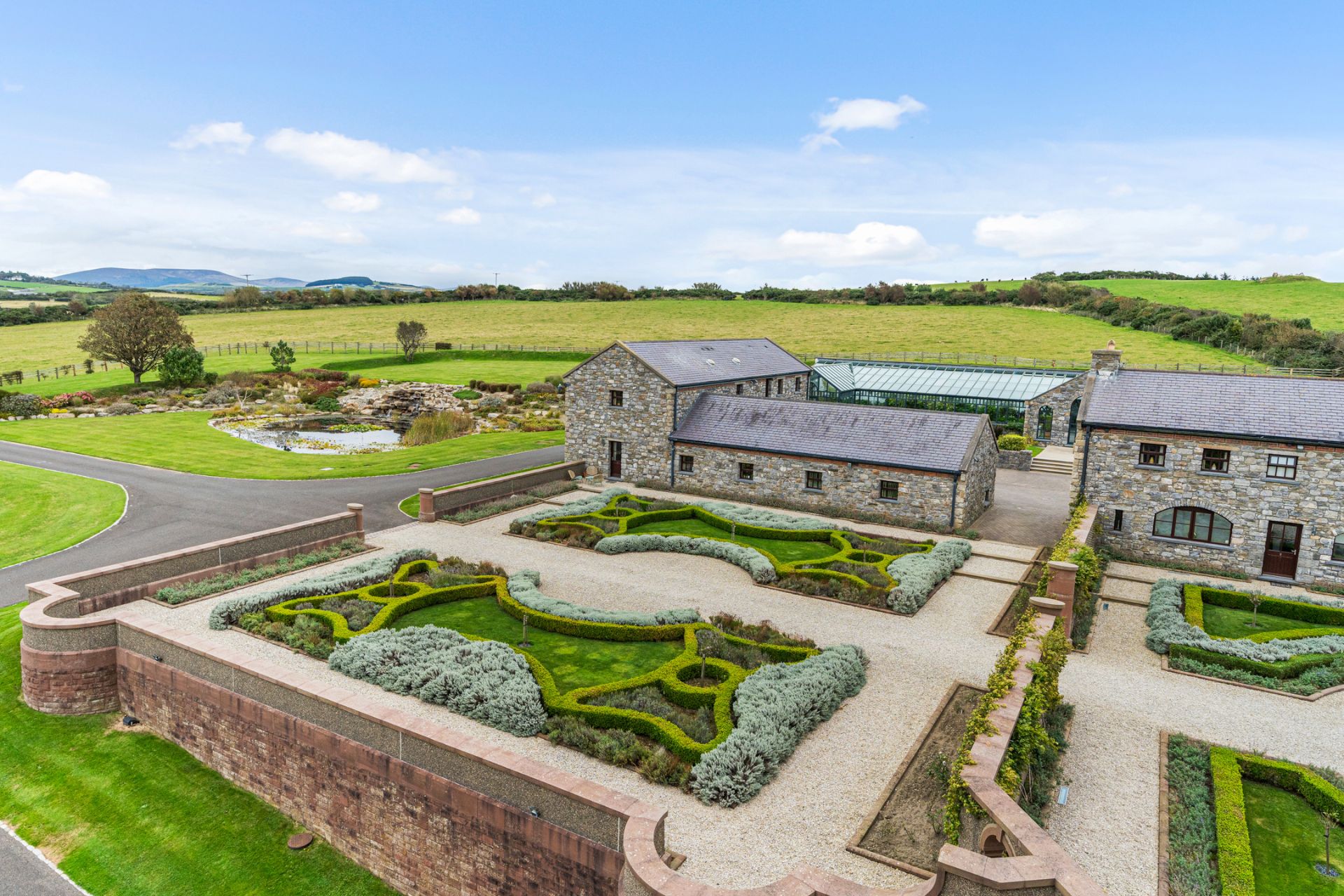 Aerial view of coastal estate with landscaped hedges, a stone cottage and a rockery