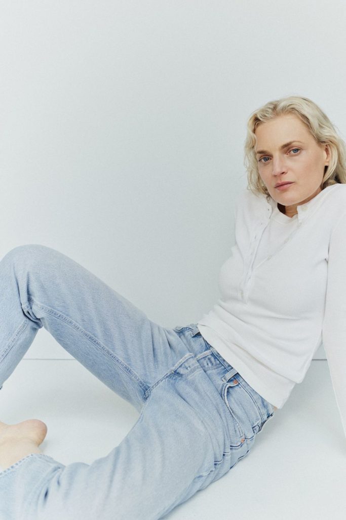 Model with short blonde hair wearing a white long-sleeve t shirt and light blue jeans