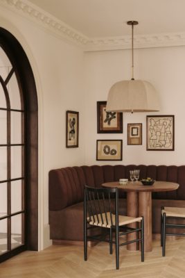 Dining nook with brown curved sofa, circular wooden table and rattan chairs.