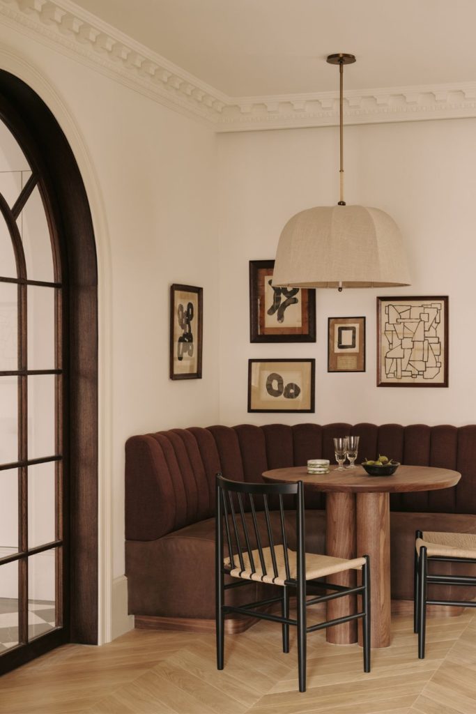 Dining nook with brown curved sofa, circular wooden table and rattan chairs.