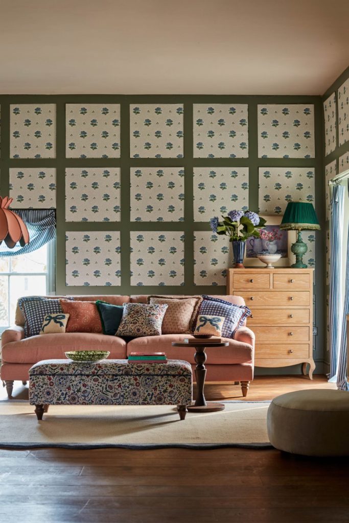 Living room with white floral wallpaper, green panelling, a pale pink velvet sofa and a blue floral footstool.