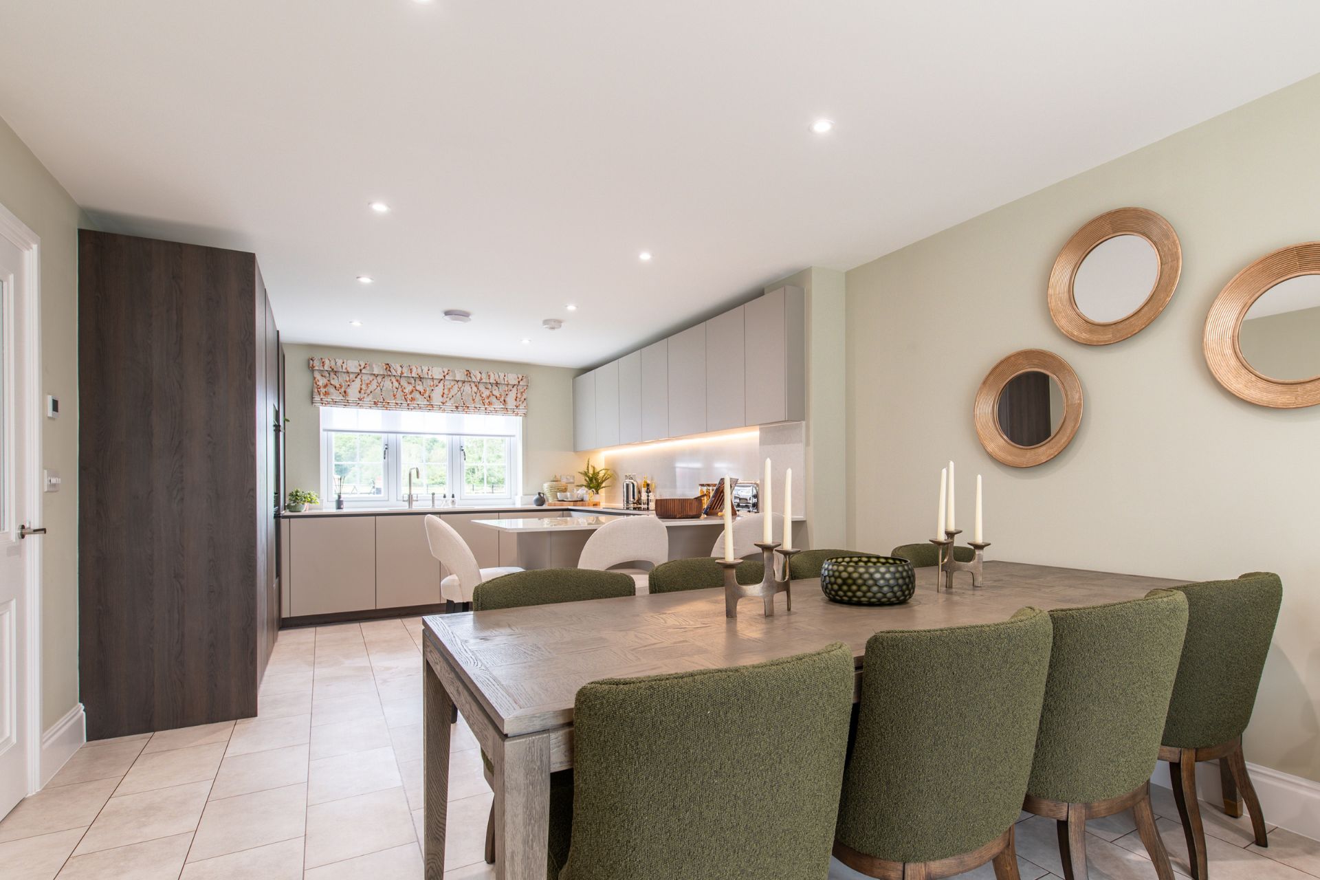 Modern kitchen with cream cabinets, dark wooden wall units, a wooden dining table and khaki dining chairs.