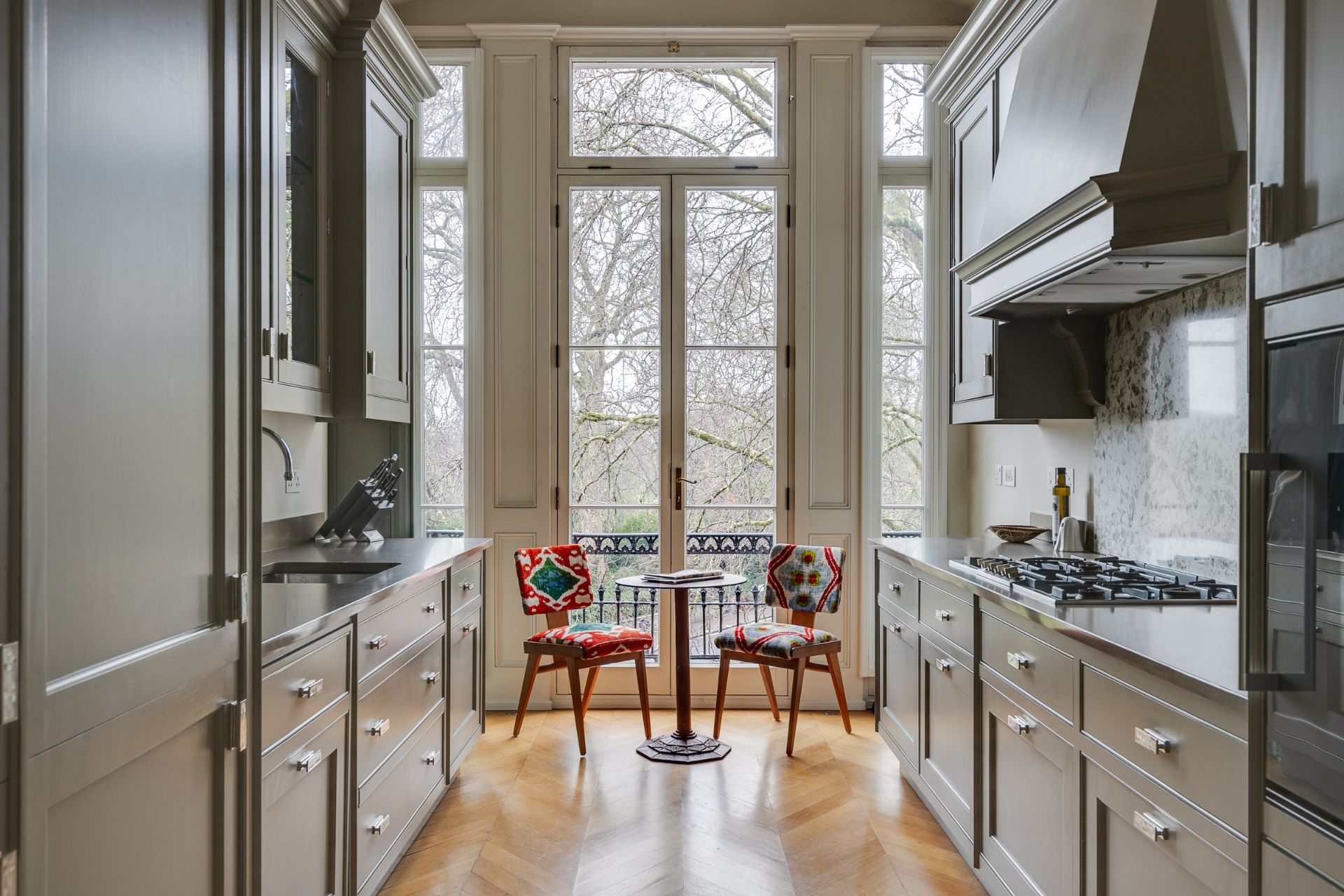 Kitchen with parquet floors, grey cabinets and colourful dining chairs.