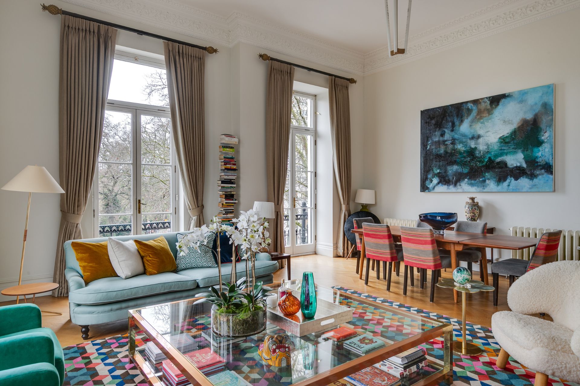 Living room with largw sash windows, parquet floors, a geometric rug and pale blue sofas.