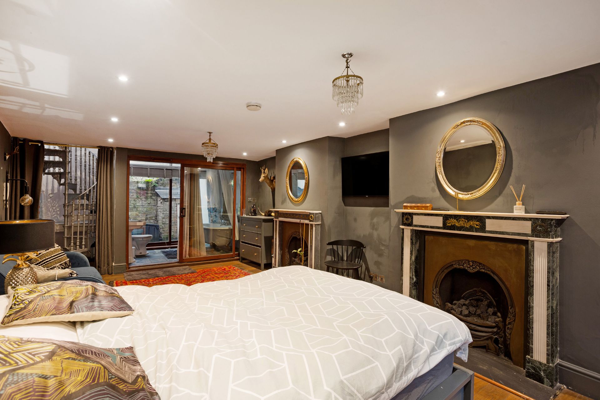 Bedroom with dark grey walls, chandeliers and round, gold-framed mirrors.