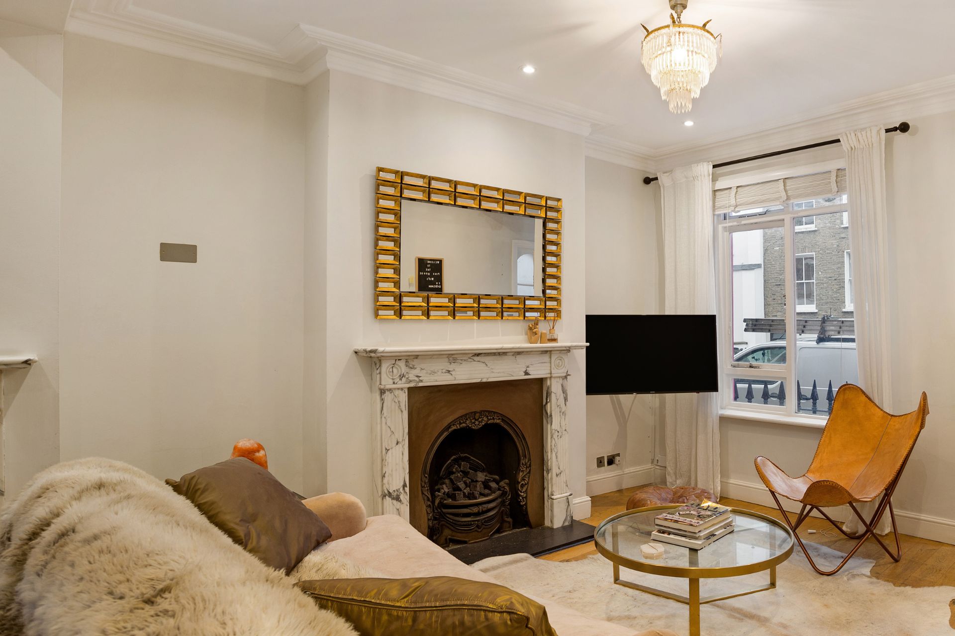 Living room with white walls, a fireplace and a taupe sofa with a fur blanket.
