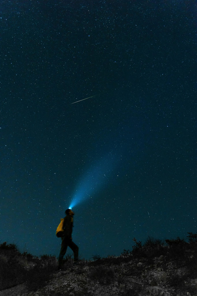 A man with a headtorch looking at a meteor in the sky