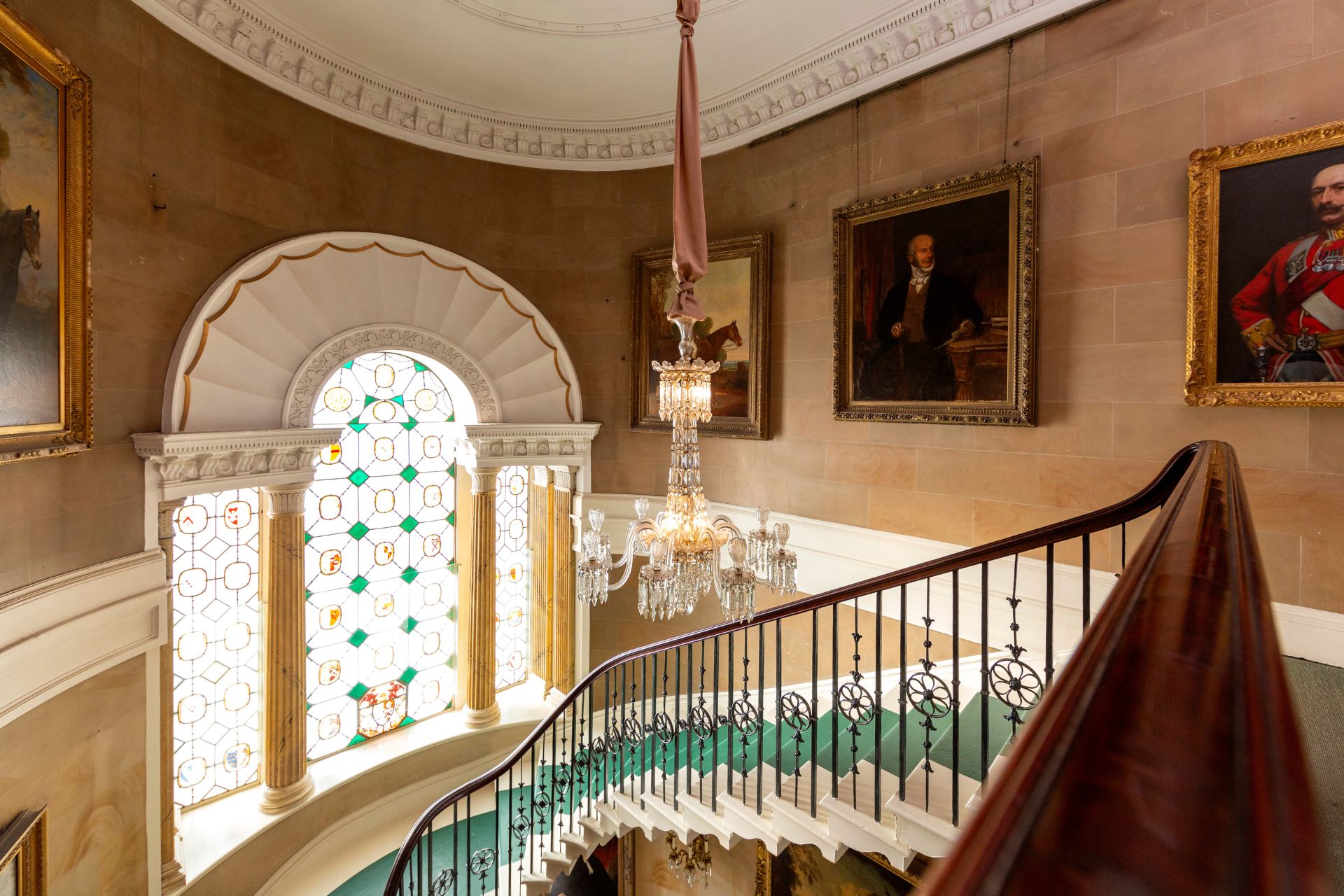 Castle staircase with arched stained glass window and chandelier above